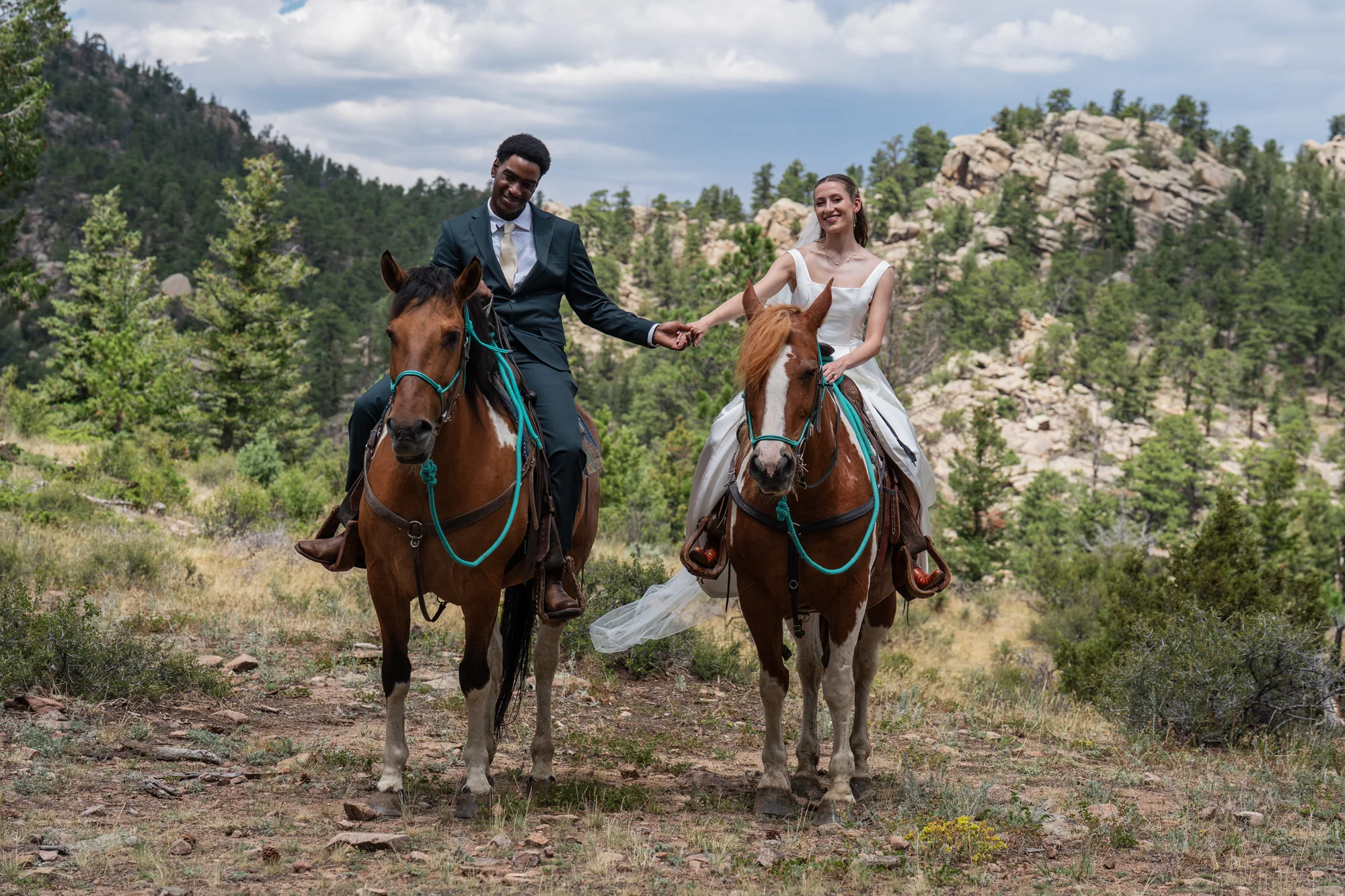 Bride and groom riding horses together through the Colorado mountains