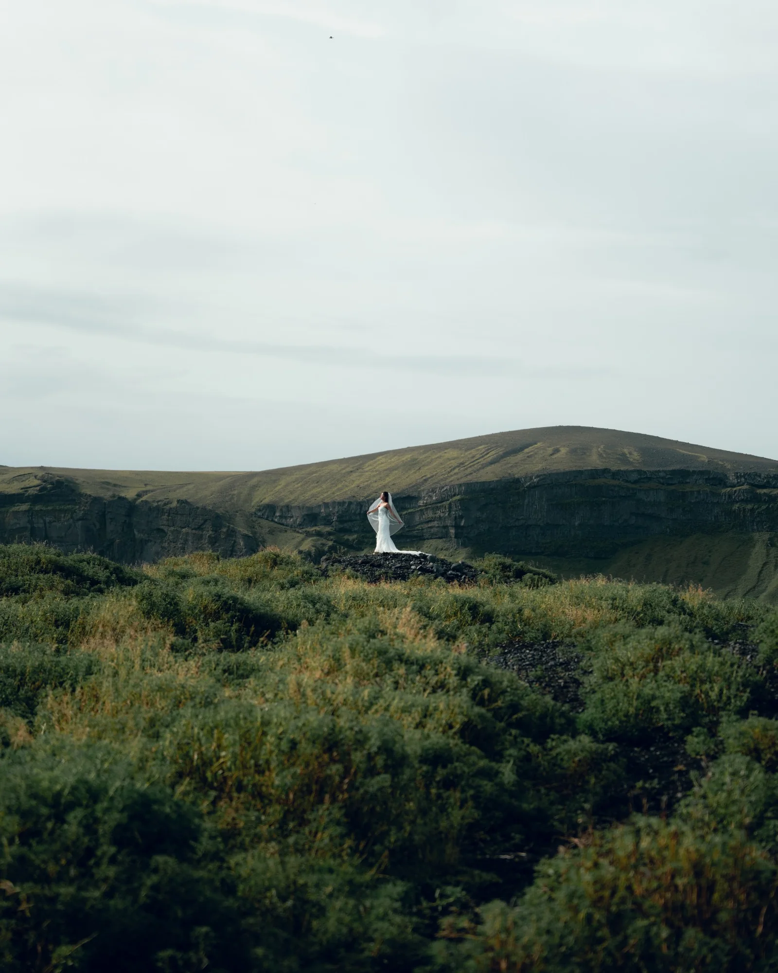 Bride in her wedding dress standing alone in the Icelandic landscape near Reynisfjara Black Sand Beach