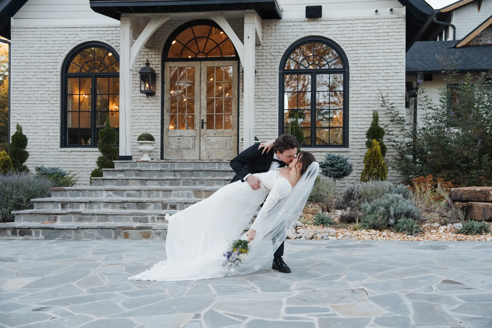 Bride and groom sharing a dip outside a white-brick wedding venue