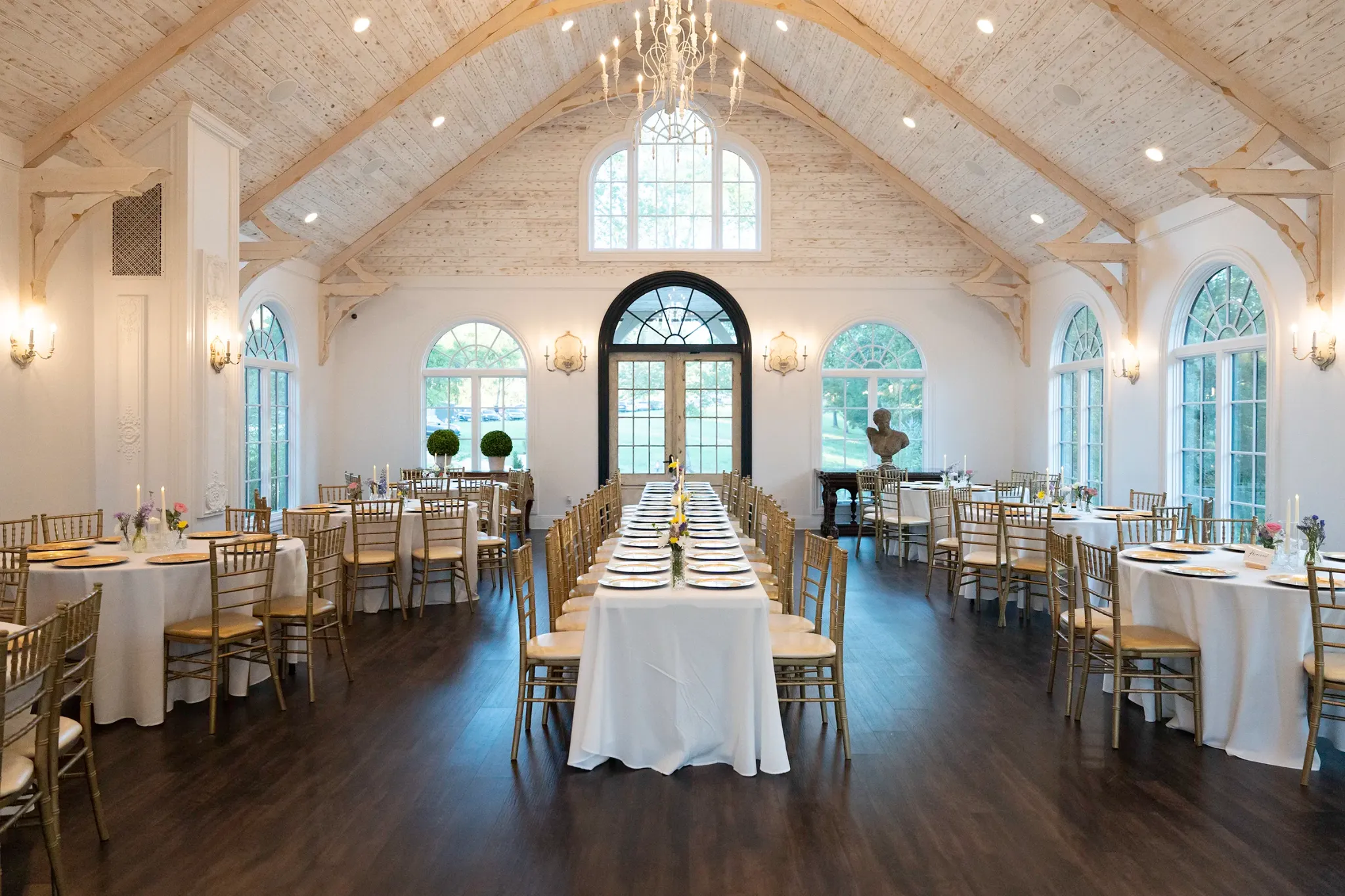Light-filled wedding reception room with long tables and gold chairs