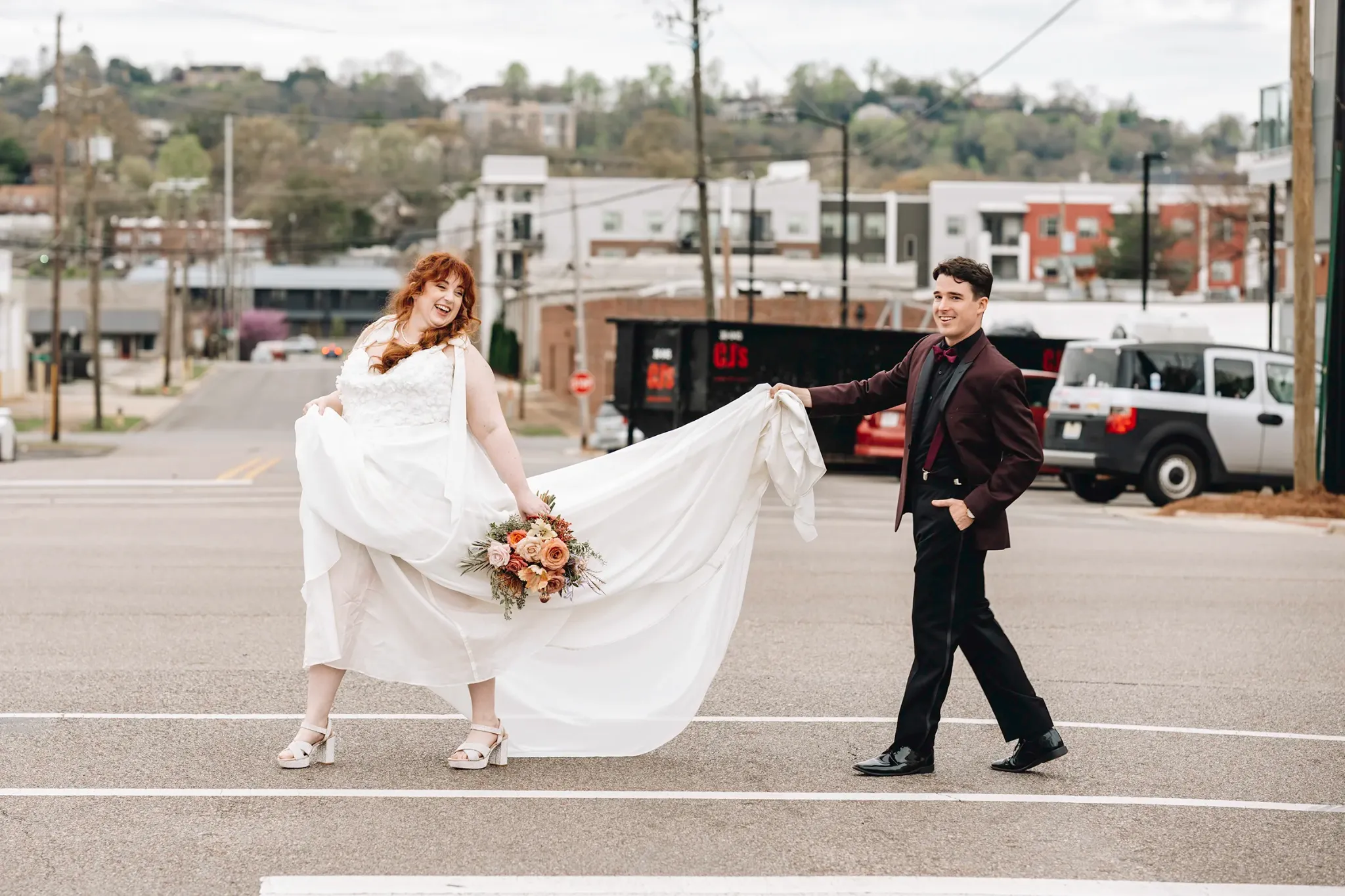 Bride and groom playfully holding the wedding dress train on a city street